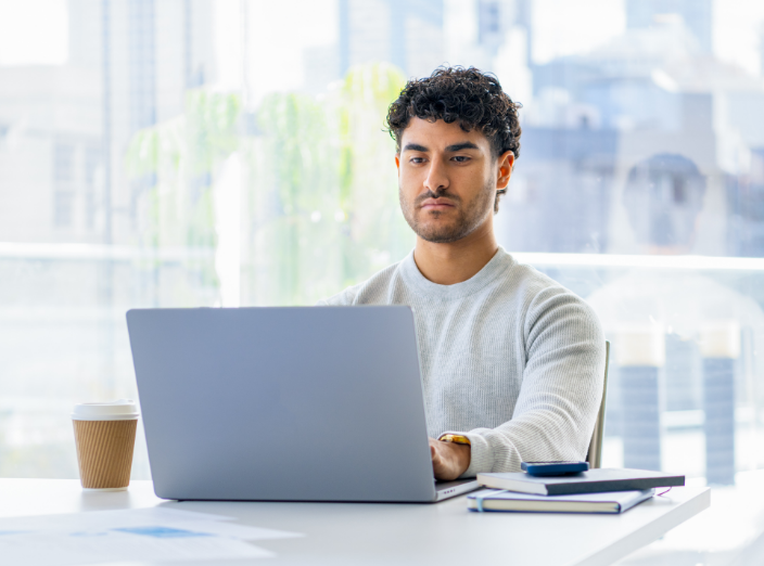 A man is sitting at a desk and working on a laptop.