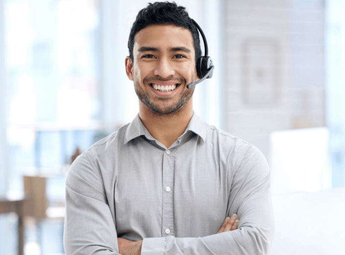 A man wearing a grey button-down shirt, wearing a headset, and smiling confidently.