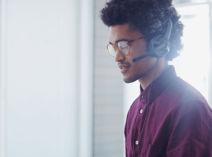 A man wearing glasses and a headset is taking a customer call.