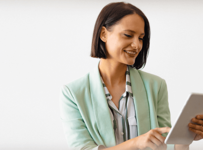 A woman in a green blazer is holding an iPad and looking at the screen.